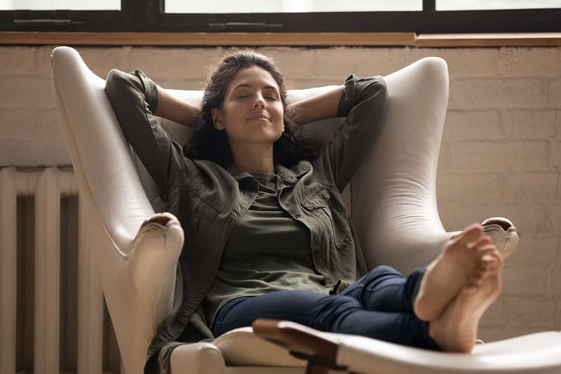 Moment de Relaxation et Bien-être dans un Fauteuil Femme souriante relaxant dans un fauteuil blanc, mains derrière la tête, profitant d'un moment de bien-être.