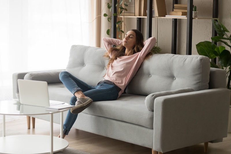 Détente et bien-être à la maison sur un canapé moderne Femme sereine se détendant sur un sofa, les mains derrière la tête après avoir travaillé sur son ordinateur portable.