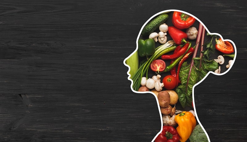 Nutrition saine et bien-être : profil femme et légumes Silhouette de profil d'une femme remplie de légumes frais colorés sur bois sombre, évoquant une nutrition saine.